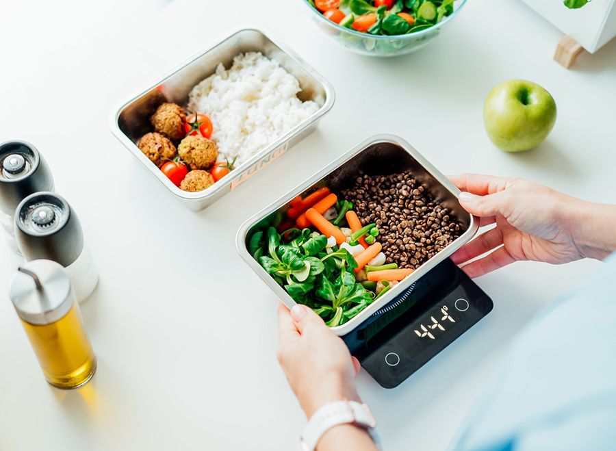 Healthy diet plan for weight loss, daily ready meal menu. Close up Woman weighing lunch box cooked in advance,ready to eat on kitchen scale. scales, weigh
