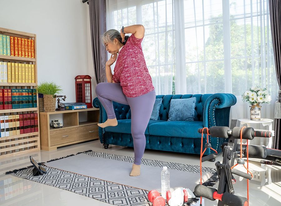Senior woman exercise with standing oblique crunch or side crunch, she watch training online in tablet during workout
