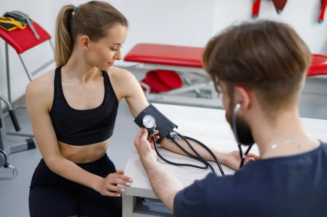 A doctor is taking the blood pressure of a woman who is wearing sportswear.