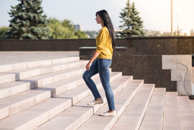 Brunette woman in a yellow sweater climbing up the stairs.