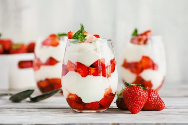 Healthy breakfast of strawberry parfaits made with fresh fruit, and yogurt over a rustic white table. Selective focus on glass jar in front. Blurred background and foreground.