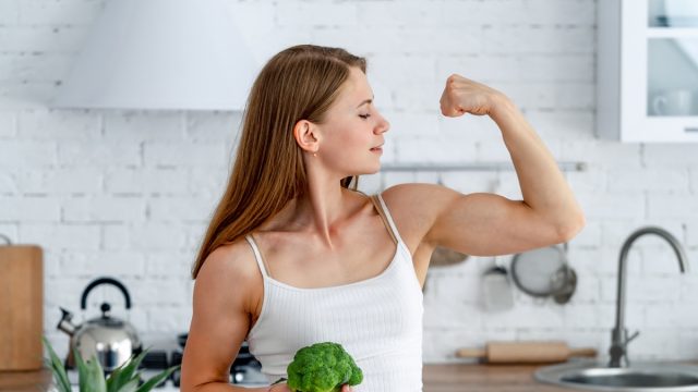Strong woman with broccoli in the kitchen