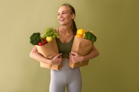 Attractive young woman holding bags of vegetables on a green background.