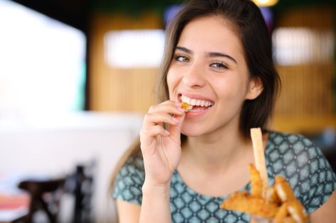 Happy woman eating chicken fingers looking at camera in a restaurant.