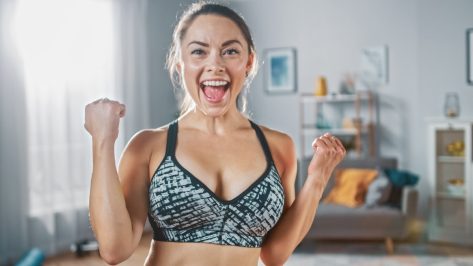 Strong and Fit Beautiful Girl in an Athletic Top is Posing After a Workout at Home in Her Spacious and Sunny Living Room with Minimalistic Interior.