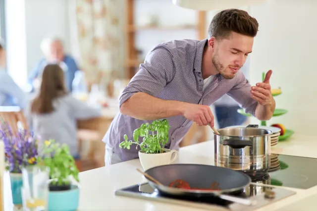 Young man with wooden spoon at pot at stove as hobby cook and houseman