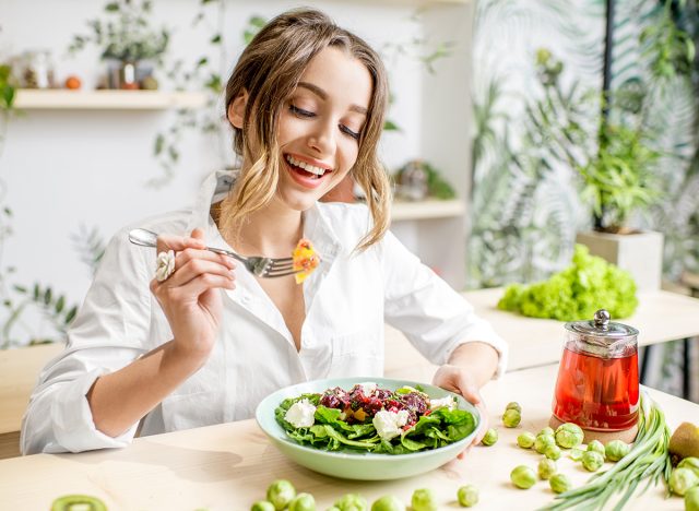 Young woman eating healthy food sitting in the beautiful interior with green flowers on the background