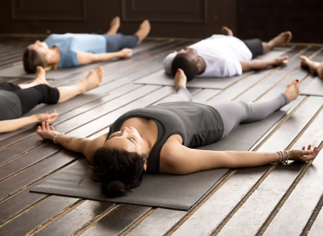 Group of young afro american and caucasian sporty people practicing yoga lesson lying in Dead Body pose, Savasana exercise, working out, resting after practice, indoor close up, studio