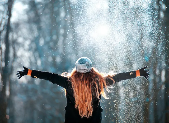 Young woman throwing snow in the air at sunny winter day, back view