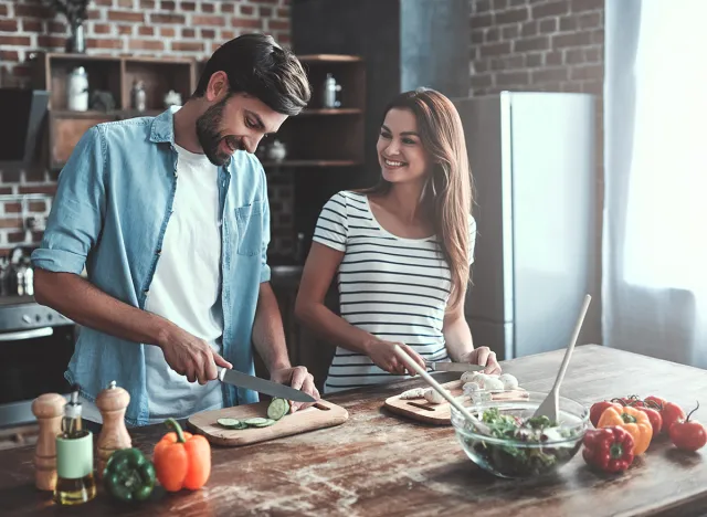 Romantic couple is cooking on kitchen. Handsome man and attractive young woman are having fun together while making salad. Healthy lifestyle concept.