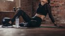 Tired woman having rest after workout. Tired and exhausted female athlete sitting on floor at gym with a water bottle.