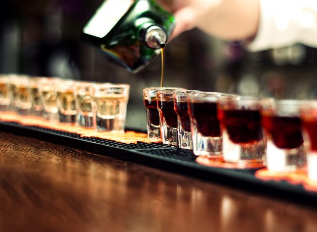 Bartender pours alcoholic drink into small glasses on bar