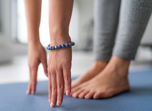 Yoga at home exercise in living room house - woman on fitness mat training stretching legs touching toes.