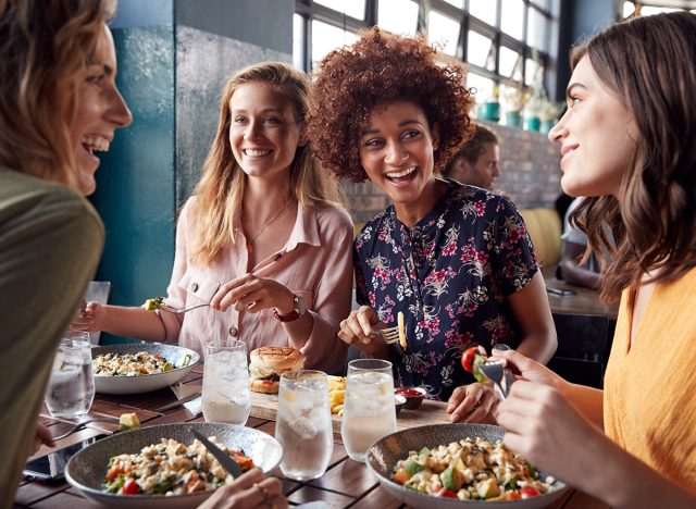 Four Young Female Friends Meeting For Drinks And Food Making A Toast In Restaurant