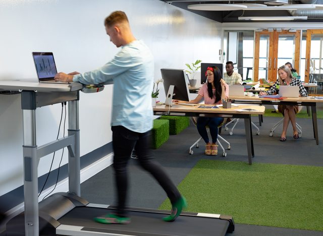Side view of Caucasian businessman working on laptop while exercising on treadmill in a modern office