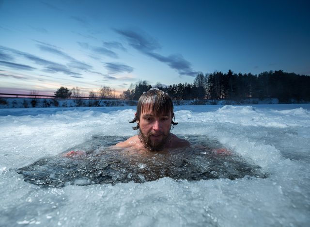 Young man with beard swims in the winter lake