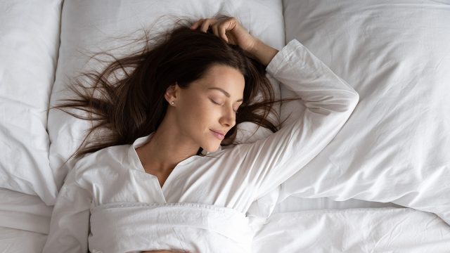 Peaceful serene beautiful young lady wear pajamas lying asleep relaxing sleeping in cozy white bed on soft pillow resting covered with blanket enjoying good healthy sleep concept, above top view