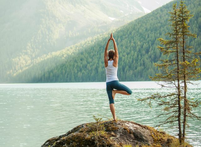 Young woman is practicing yoga at mountain lake