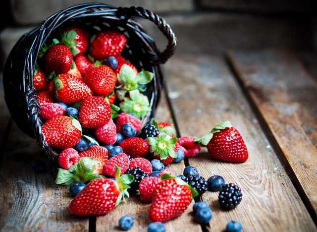 Mix of fresh berries in a basket on rustic wooden background