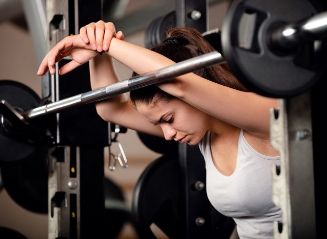 Very beautiful teenage girl resting and getting motivated between sets of barbell squats in gym. She keeps her eyes closed.