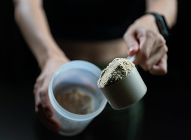 Close up of women with measuring scoop of whey protein and shaker bottle, preparing protein shake.