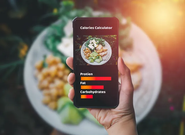 Smartphone and calories calculator concept. Hand holding smartphone and take photo of chicken grill, avocado, chickpea, cheese and lettuce in white salad plate. In vintage tone
