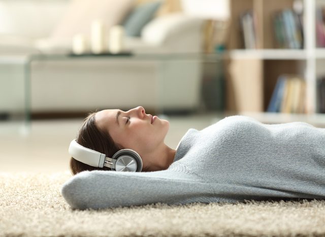 Side view portrait of a relaxed woman listening to music with headphones lying on a carpet at home