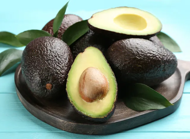 Board with whole and cut avocados on turquoise table, closeup