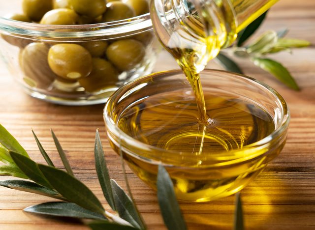 The moment olive oil is poured into a glass bowl set against a wooden background