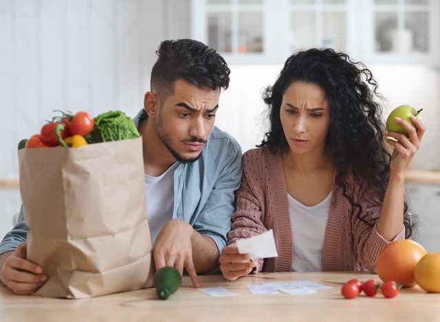 Frustrated Arab Spouses In Kitchen Checking Bills After Grocery Shopping, Young Middle Eastern Couple Sitting At Table And Counting Spends, Confused By Big Prices And Food Expenses, Closeup Shot
