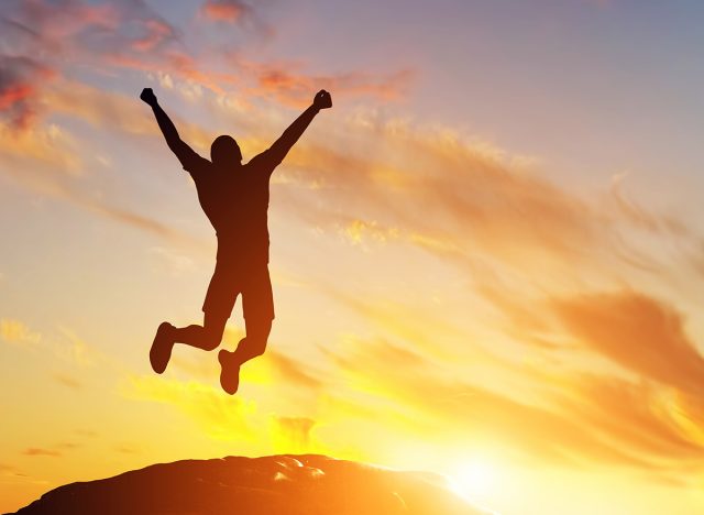 Happy man jumping for joy on the peak of the mountain, cliff at sunset. Success, winner, happiness