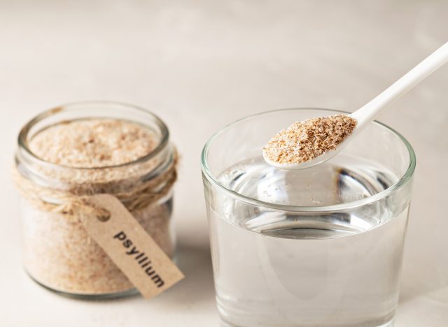 Plantain husk in a jar with the inscription psyllium and a glass of water on a light background.