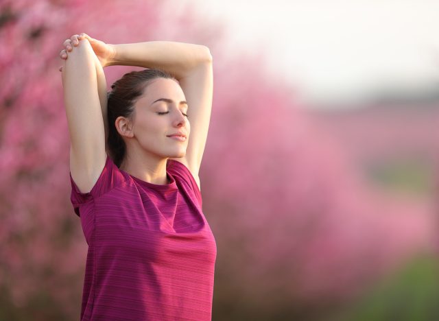 Sportswoman stretching arms and relaxing in a field after sport