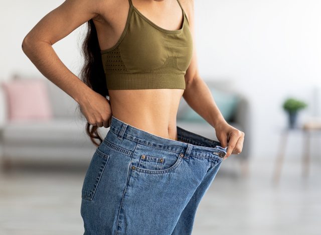 Successful weight loss diet concept. Cropped view of young Indian lady in big jeans demonstrating results of her slimming program, promoting healthy eating at home, closeup