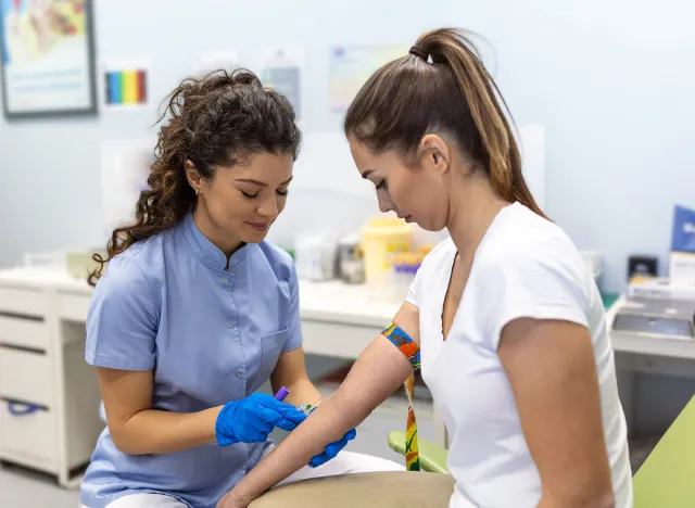 Preparation for blood test with pretty young woman by female doctor medical uniform on the table in white bright room. Nurse pierces the patient's arm vein with needle blank tube.