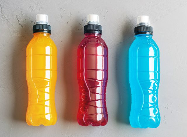 Flat lay shot of three bottles of orange, red and blue isotonic drink on a grey concrete background