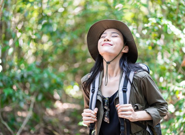 Asian young beautiful female backpacker traveling alone in forest wild. Attractive girl traveler look around and explore while walk in nature wood with happiness and fun during holiday vacation trip.