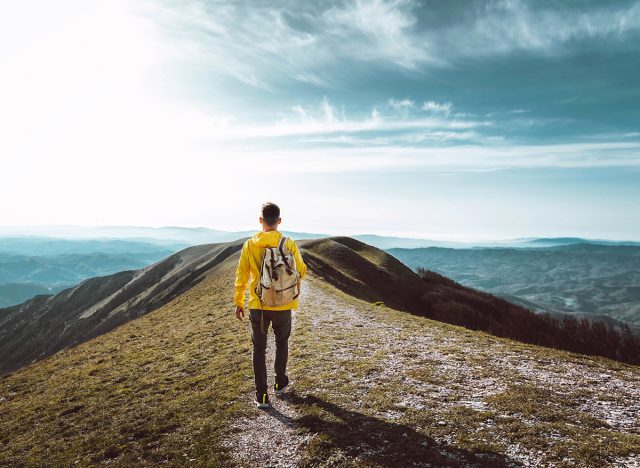 Young man with backpack hiking mountains - Hiker having trekking day out on a sunny day - Successful, sport and inspirational concept