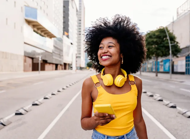 Beautiful young happy african woman with afro curly hairstyle strolling in the city - Cheerful black student walking on the streets