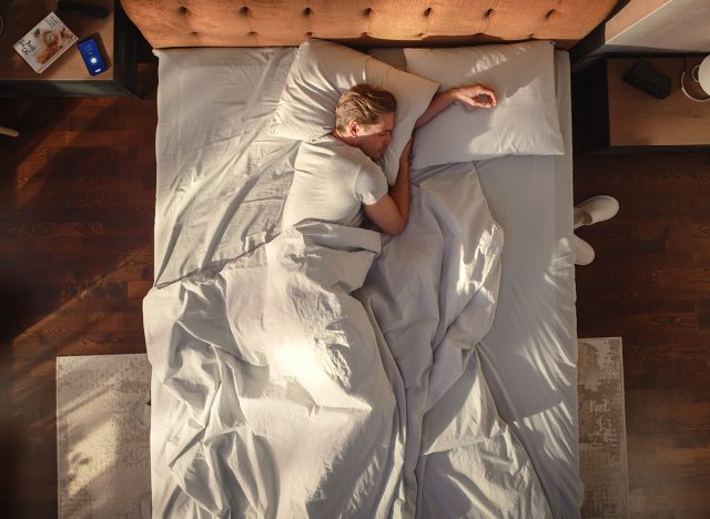 Top View Home: Handsome Young Man Sleeps in His Bed in a Stylish Bedroom, Sun Shines on Him. Morning Concept. Peaceful Sleeping and Relaxation, Important for Wellness . Top Down Above Shot