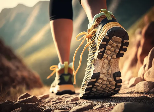 Hiking in the mountains. Female legs with sports shoes and backpack running on a trail mountain, close up