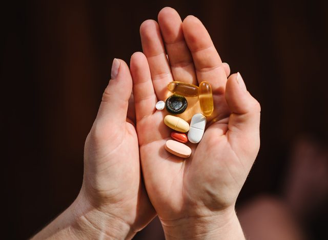 Woman hands with omega 3, multivitamins, vitamins B, C, D, collagen tablets, probiotics, iron capsule. Hand hold supplements on blurred background. Unrecognizable woman takes vitamins daily. Top view.