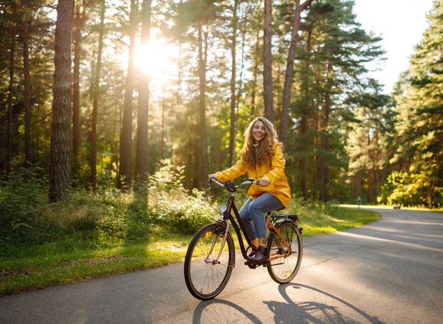 Young happy woman in a yellow coat rides a bicycle in a sunny park. Beautiful woman enjoys autumn nature. Relax, nature concept. Lifestyle.