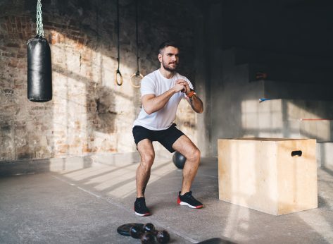 Full length of muscular man in sportswear doing squats during intense training at modern sports center with fitness equipment for workout