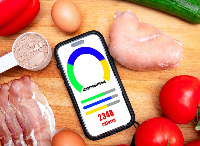 phone with calorie and macronutrient counting app on phone next to healthy food. Healthy diet and maintaining a caloric deficit