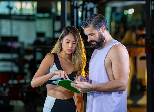 Gym customer is getting advice and suggestion from her personal trainer for exercising plan program and getting her evaluation chart from sample blood test for her workout progress concept