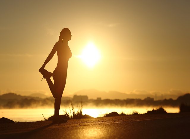 Silhouette of a fitness woman profile stretching at sunrise with the sun in the background
