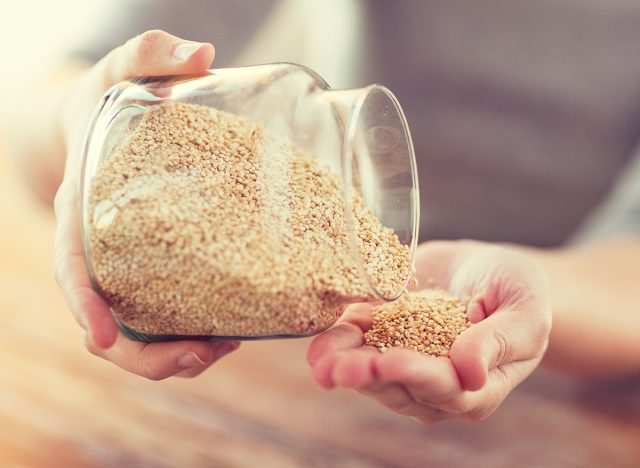 cooking and home concept - close up of female emptying jar with quinoa