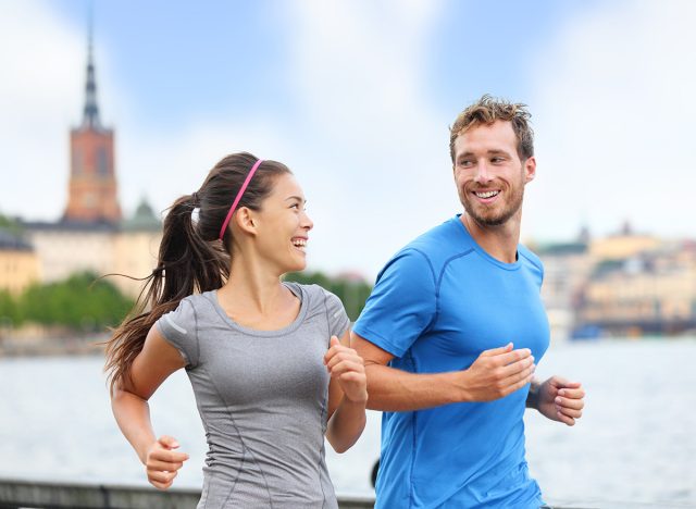 Healthy runners running in Stockholm city cityscape background. Riddarholmskyrkan church in the background, Sweden, Europe. Healthy multiracial young adults, asian woman, caucasian man.