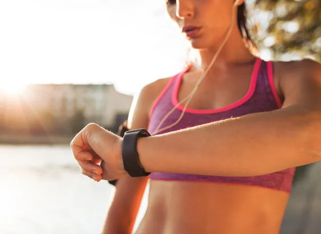 Young fitness woman looking at her smart watch while taking a break from outdoor workout. Sportwoman checking pulse on fitness smart watch device.